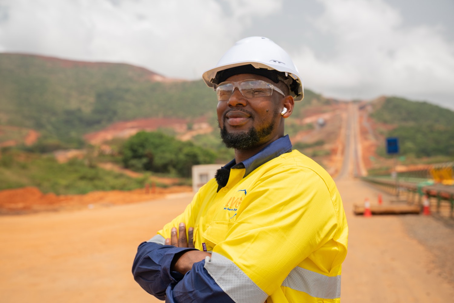 Ousmane, LVG's Managing Director, wearing high-visibility PPE, on a Simandou project site with the hills in the background.