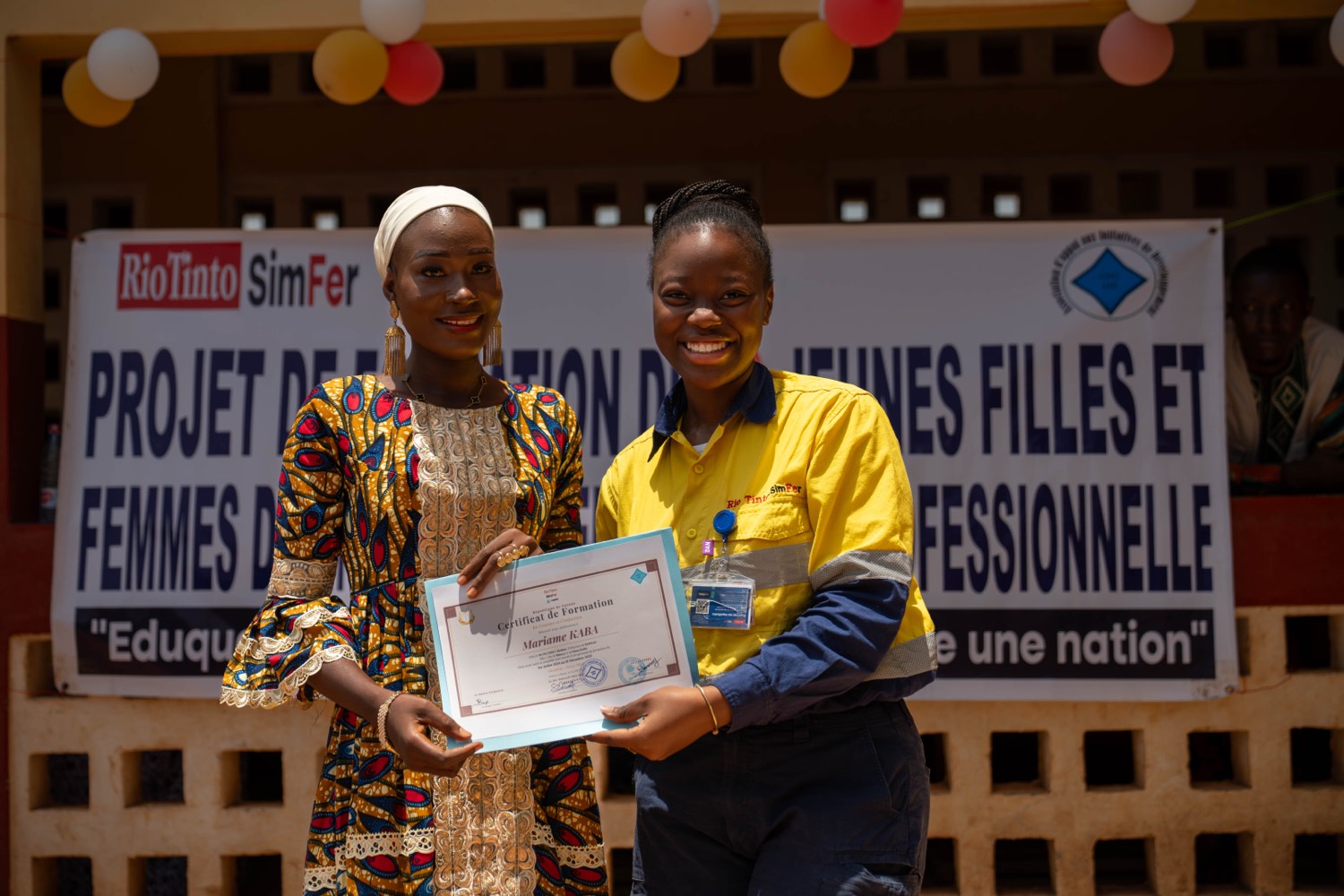 Une diplômée reçoit son certificat devant la bannière du projet Rio Tinto SimFer de formation des jeunes filles et femmes