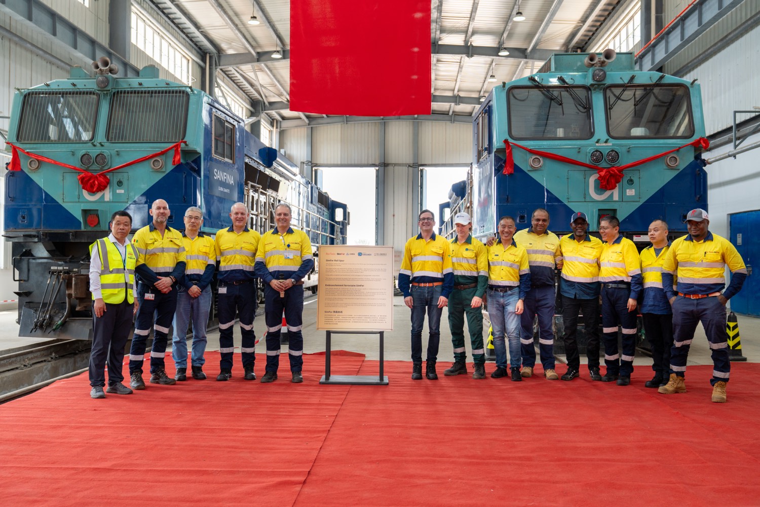 L’équipe de SimFer lors de la cérémonie célébrant l’achèvement de l’embranchement ferroviaire, devant deux locomotives SimFer.