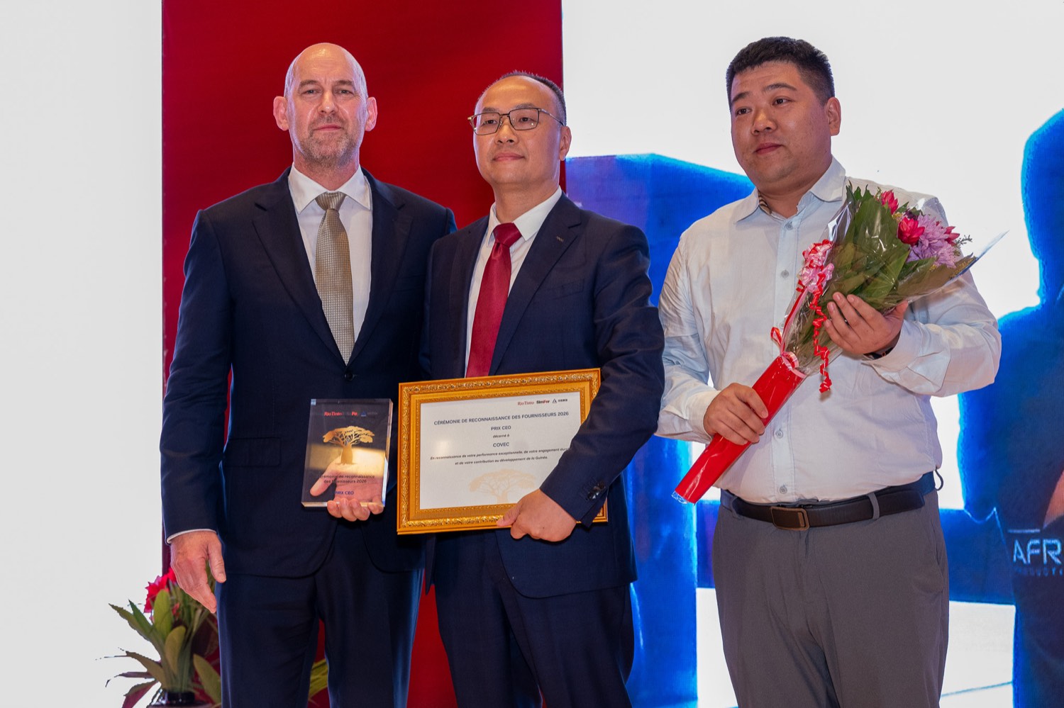 Chris Aitchison, SimFer Managing Director, presenting the CEO Award framed certificate to Liu Chenyu of COVEC, alongside a COVEC representative holding flowers.