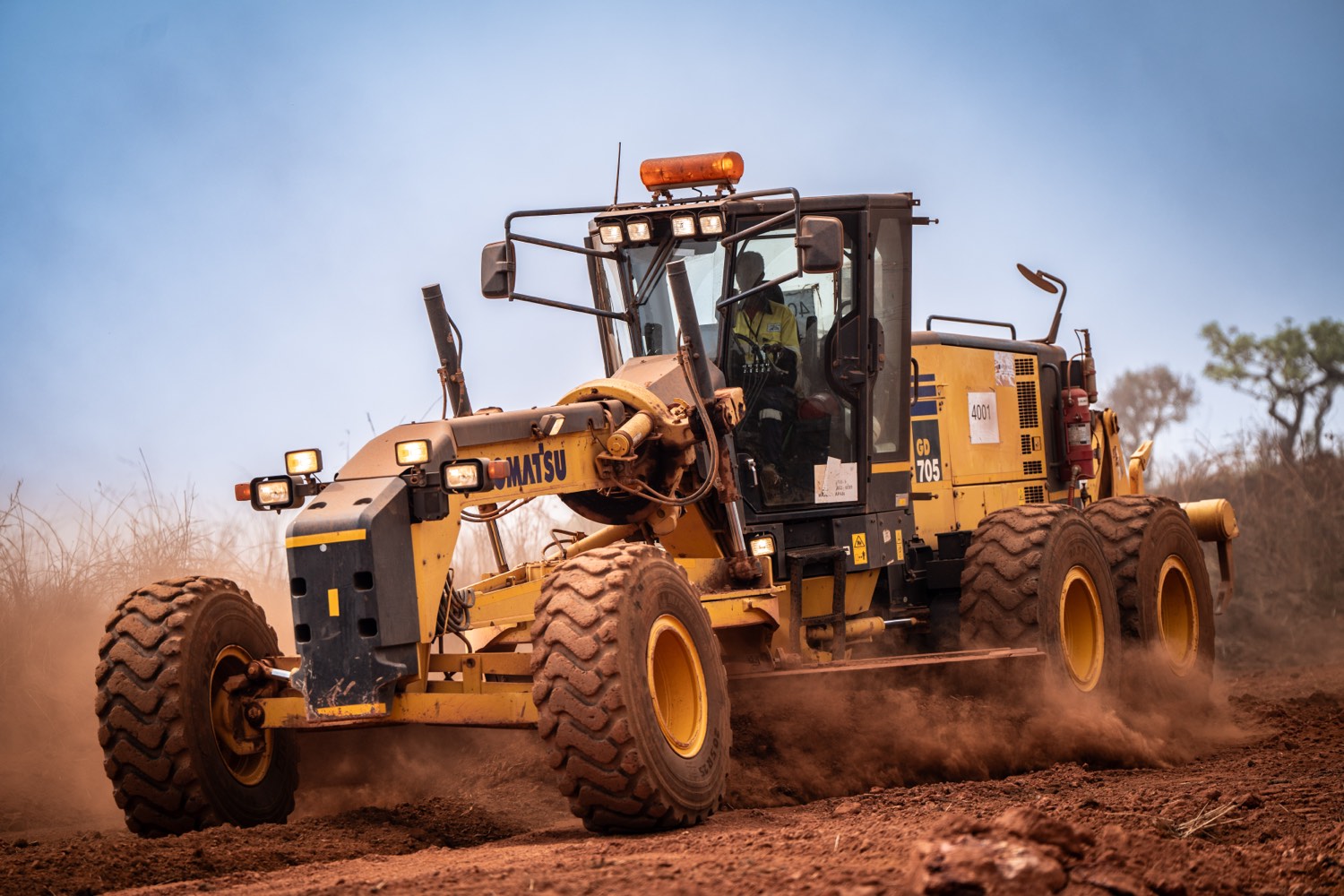 Une niveleuse Komatsu GD705 en opération sur une piste poussiéreuse du site de Simandou